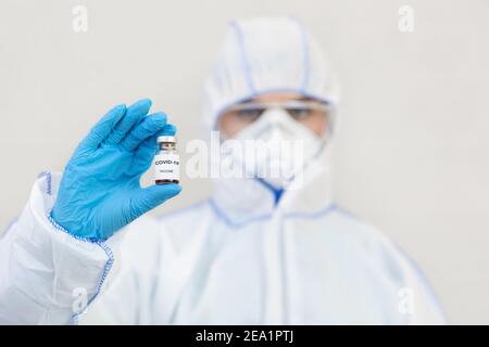 Medic in hazmat suit, gloves, protective mask and goggles holds vaccine against Covid-19 Stock Photo