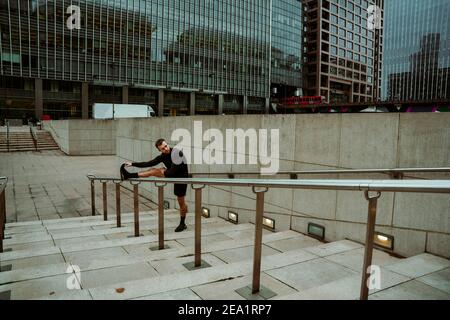 Caucasian male athlete stretching legs while on outdoor run training for marathon in city Stock Photo