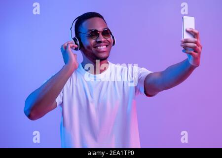 Handsome Black Man Wearing Wireless Headphones And Sunglasses Taking Selfie On Smartphone Stock Photo