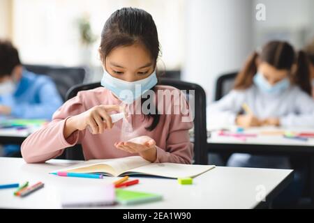 Small asian student applying antibacterial sanitizer on hands Stock Photo