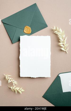 White and green wedding stationery set. Blank greeting card, craft envelope with wax seal stamp, dried flowers. Flat lay, top view, vertical. Stock Photo