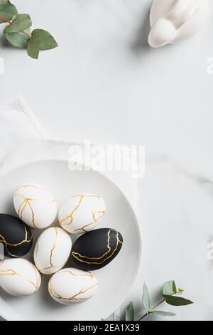 Happy Easter concept. Luxury Easter eggs, bunny rabbit, eucalyptus leaves on marble table. Flat lay, top view, vertical. Stock Photo