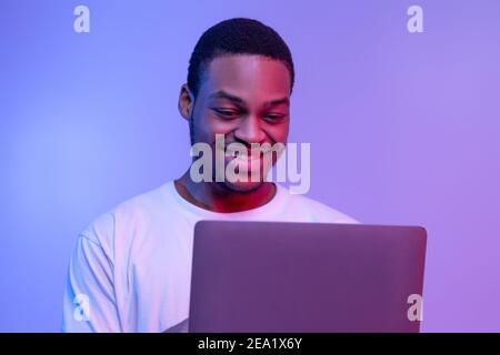 Handsome Smiling Black Programmer Guy Working Online On Laptop In Neon Light Stock Photo