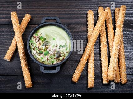 Avocado dip (hummus) with nibbles arranged on brown wooden background, text free space Stock Photo