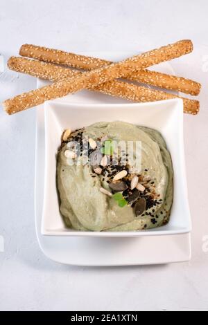 Avocado dip with sunflower seeds and pumpkin seeds, served in a white porcelain dish on a white background, with sesame sticks Stock Photo