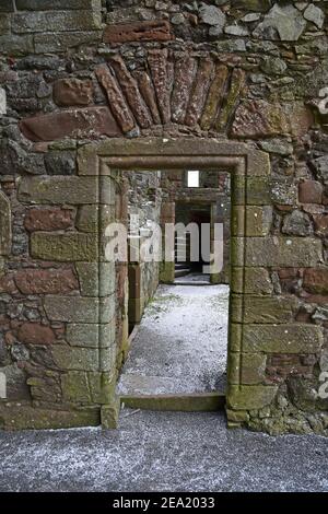 Architectural detail of ruined Balvaird Castle in Scotland showing doorway leading to passageway and spiral stone staircase. Snow on ground. Stock Photo