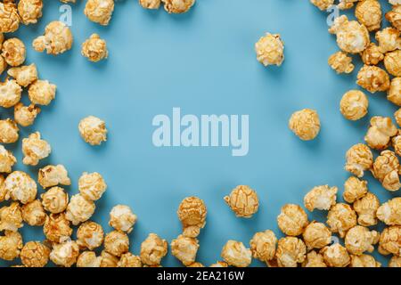 Popcorn is scattered on a blue background, in the form of a frame. Yummy for the filming of movies, TV series, cartoons. Free space, top view Stock Photo