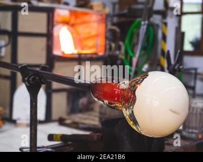 Detail of blowing molten glass into a dish during an art show and traditional craft demonstration. The shining open glass kiln in background of worksh Stock Photo