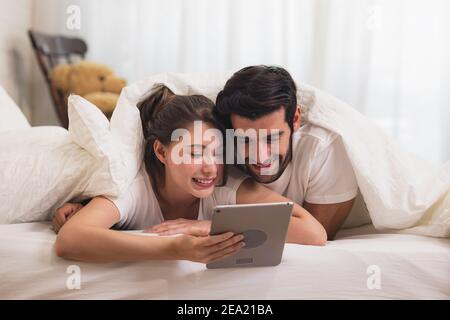 Close up Young Sweet Couple on Bed Watching Something on Tablet Gadget, relaxing in bedroom. Stock Photo