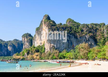 Holidaymakers enjoy the beach and sea under the shadow of a huge rock formation on Railay Beach, near Krabi, Thailand Stock Photo