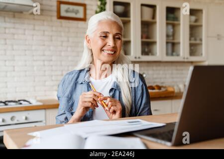 Confident smiling mature business woman sitting at home with laptop and talking with partners online Stock Photo