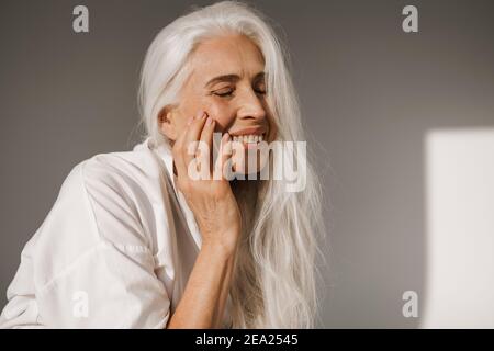Joyful elderly white-haired woman laughing at camera isolated over grey background Stock Photo
