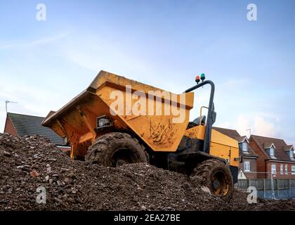 Mini yellow dumper with roll bar and orange flashing lights tipper front bucket  parked on construction mound of soil on new houses industrial site Stock Photo