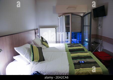 Room interior is in an inexpensive hotel in Lyon in France in the evening. Two beds iare n the foreground and blinds to the floor are against the back Stock Photo