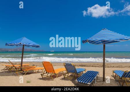 Crete beach Kalyves. Blue and yellow umbrellas and sunbeds against the backdrop of a beautiful blue sea on a sunny day. Public beach Kalyves in Crete Stock Photo