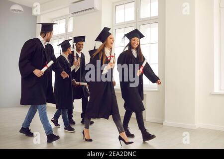 Group of multiracial university graduates walk down the hall with diplomas in hand. Stock Photo