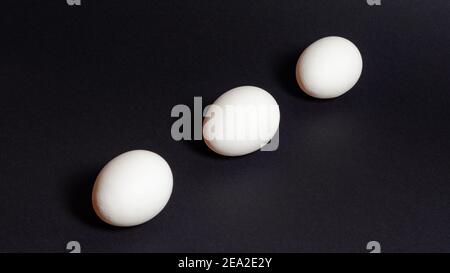 Three white eggs on a black background, dietary and healthy food rich in protein 2021 Stock Photo