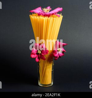 Italian pasta, spaghetti in a glass on a black background, decorative purple flower 2021 Stock Photo