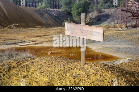 Blank sign on top of chemical waste pile with an abandoned mine quarry and rusty machinery, selective focus Stock Photo