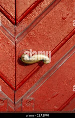Close up of old brass door handle on a weathered red wooden door with profiles. Stock Photo