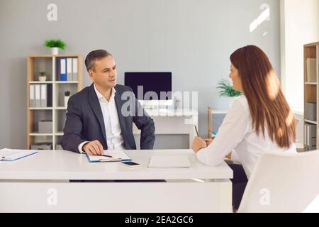Male and female office workers sitting at a desk and discussing office workflows. Stock Photo