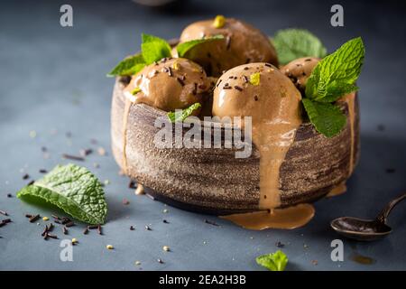 Scoops of coffee or chocolate ice cream in a bowl with green leaves on dark background Stock Photo