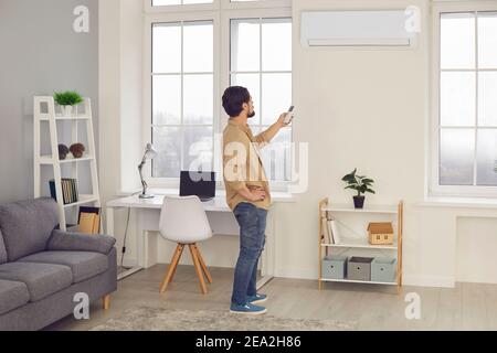 Man standing in living-room and adjusting air conditioner settings with remote control Stock Photo