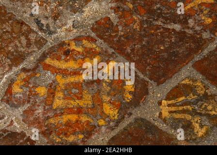 The fleur-de-lis, the lily flower emblem of the French monarchy, features with other heraldic devices as the rich yellow motif on orange-red medieval inlaid or encaustic tiles in the pavement of the Gothic Cathédrale Notre-Dame de Laon at Laon, Aisne, Hauts-de-France, France - despite centuries of wear, tear and the passage of thousands of feet.  Laon Cathedral was built in French Gothic style in the 12th and early 13th centuries. Stock Photo