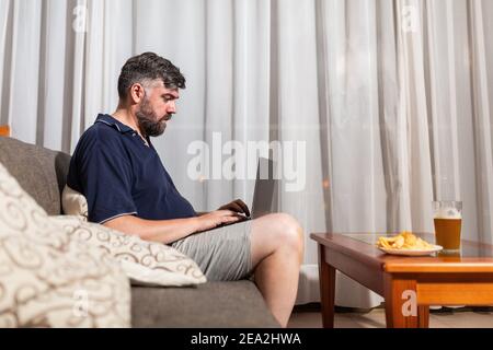 bearded man on sofa uses laptop in dining room overnight Stock Photo