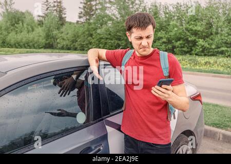 discontented and frustrated man tries to book a car in a car sharing service or calls a taxi using an app on his smartphone Stock Photo