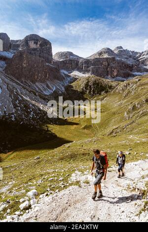 Hikers in the Zwischenkofel valley with the Antersasc alpine pasture below the Puez peaks in the morning sun, Dolomites Puez-Odle Group, South Tyrol Stock Photo