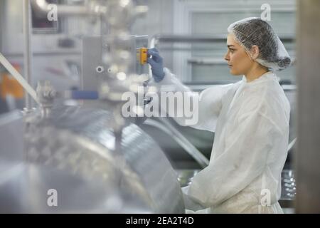 Side view portrait of female worker pushing button while operating machine units at clean food production factory, copy space Stock Photo