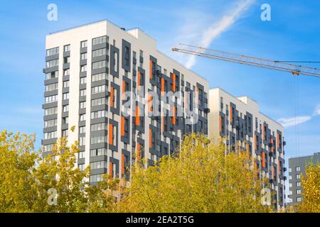 Modern apartment building is in street 800letie Moscow. Building is on the background of a tower crane boom and yellow trees. Concept renovation. Mosc Stock Photo