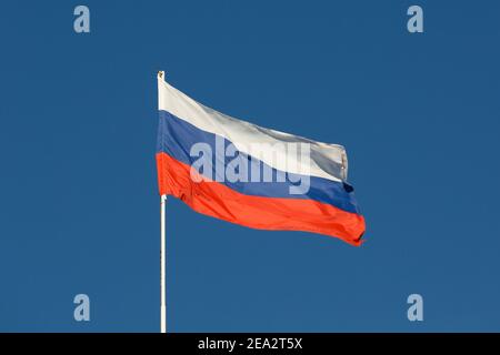 Russia flag is on a pole against a blue sky.  The Russian flag flies in the wind. Stock Photo