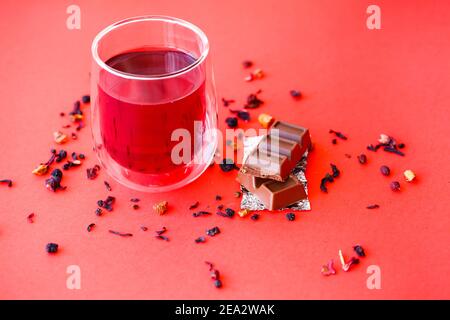 Hot hibiscus tea in a transparent glass with a double bottom on a red background Stock Photo