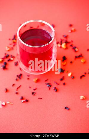 Hot hibiscus tea in a transparent glass with a double bottom on a red background Stock Photo