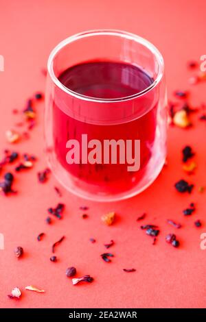 Hot hibiscus tea in a transparent glass with a double bottom on a red background Stock Photo