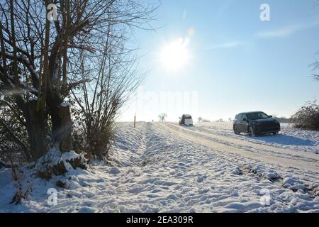 Road with cars in the country, with a lot of snow in winter, with tree, blue sky and sun Stock Photo