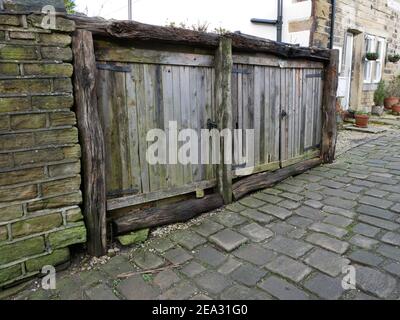 Cobbled hillside road old decaying short wooden doors with rough rotting logs framing by stone wall and houses Stock Photo