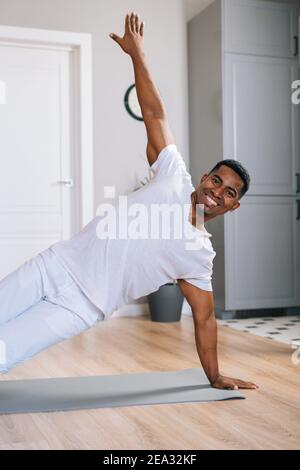 Cheerful sporty African-American man exercising in side plank position on floor during working out. Stock Photo
