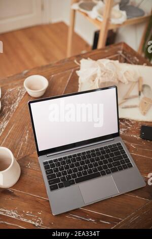 Vertical background image of laptop with blank white screen on table in workshop, small business and entrepreneurship concept, copy space Stock Photo