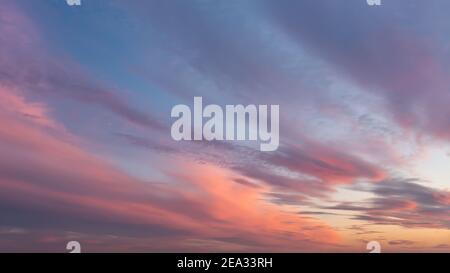 Dramatic vanilla skyscape. Purple orange sunset clouds against blue sky. Scenic dynamic low clouds in a twilight heaven. Stock Photo
