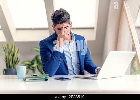 Shot of exhausted businessman with hands on his forehead sitting in the office. Professional man having pain in his head. Stock Photo