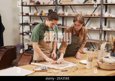 Portrait of young woman teaching apprentice making ceramics in pottery workshop, copy space Stock Photo