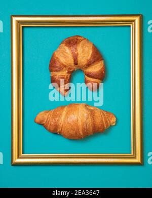 Two different croissants in golden frame on turkis background. Butter fresh made pastries. Flat lay concept, simple Stock Photo