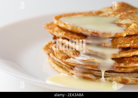 Plate with pancakes and condensed milk served on table. Dairy product. Delicious homemade breakfast Stock Photo