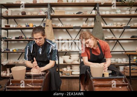 Front view portrait of two young people shaping clay on pottery wheels while enjoying hobby in workshop, copy space Stock Photo