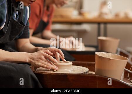 Side view close up of female hands shaping clay on pottery wheel in workshop while enjoying arts and crafts, copy space Stock Photo