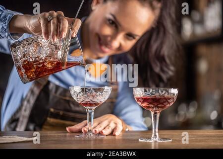 Female bartender pours manhattan cocktail into an ornamental glass. Stock Photo