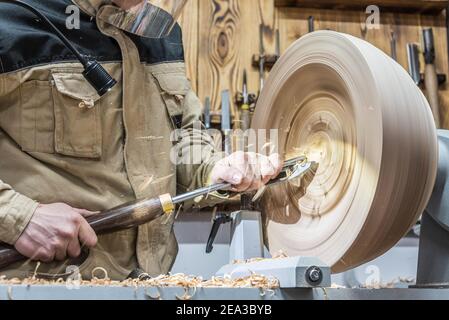 Turning wooden bowls on a lathe. The close up view of spinning the lathe machine. Man with a chisel and shavings flying off. Stock Photo